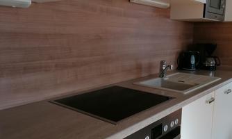 A modern kitchen with white cabinets and a wooden backsplash. It is equipped with a cooktop, a sink, and appliances such as a refrigerator and a microwave.