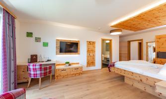 A modern room with wooden furniture and a large bed. The space is bright and inviting, with a TV and a small desk.