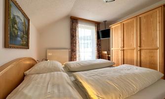 A cozy bedroom with a large double bed and bright wooden wardrobes. The windows let in natural light and a beautiful landscape picture frames the wall.