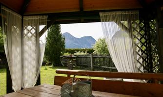 A cozy porch with a wooden bench and a view of the mountains. Soft curtains and green grass create an inviting atmosphere.