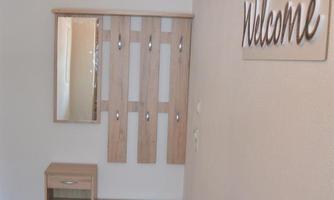An inviting hallway with a wooden cabinet and a mirror. On the wall hangs a sign that reads "Welcome".