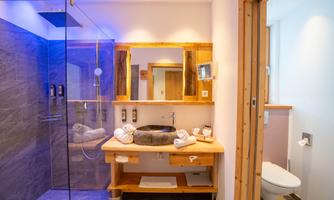 A modern bathroom with a spacious shower and a wooden sink shelf. The lighting and the use of natural materials create a relaxed atmosphere.