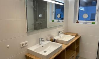 A modern bathroom with two ceramic sinks. The room is bright and has a window front that lets in daylight.