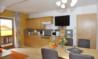 A modern kitchen with wooden cabinets and a dining area. The room is bright and friendly with access to a balcony.