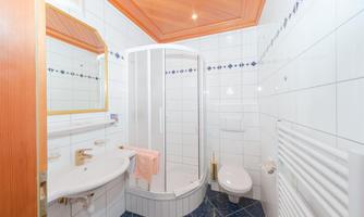 A modern bathroom with a shower, a sink, and a toilet. The walls are tiled and the ceiling has a wood design.
