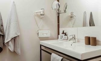 A modern bathroom with a washbasin, a mirror, and two towels. On the countertop are placed toiletries and two cups.
