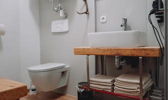 A modern bathroom with a white toilet and an elegant sink on a wooden shelf. Towels are neatly stacked and there are other bathroom accessories.