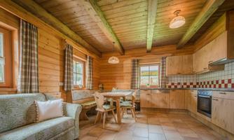 A cozy wooden apartment with an open kitchen and a dining area. The warm colors and wooden beams create an inviting atmosphere.