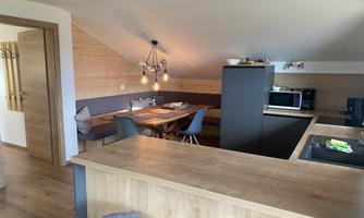 A modern kitchen with wooden details and a dining area. Large windows provide plenty of natural light and a welcoming atmosphere.