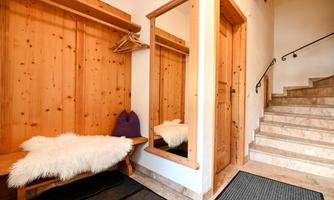 An inviting hallway with wood paneling and a large mirror. A staircase leads upstairs and on a bench lies a soft fur.
