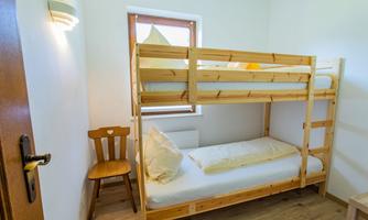 A simple room with a bunk bed and a chair. It has light-colored walls and a small window view.
