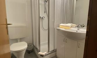 A modern bathroom with a shower and a sink. There is also a toilet and bright lighting.