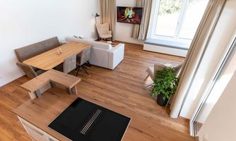 A modern living room with wooden floor and large window. There is a seating area, a dining table, and a television above a fireplace.
