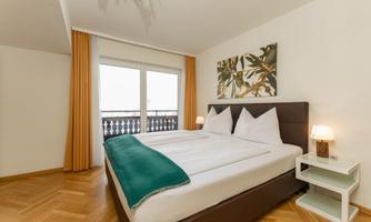 A modern bedroom with a large double bed and bright curtains. The room is friendly and inviting, with a beautiful piece of artwork on the wall.