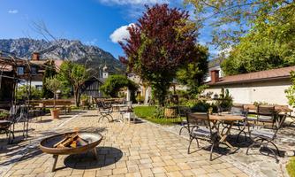 An inviting outdoor area with tables and chairs, surrounded by trees and a picturesque mountain backdrop. Ideal for relaxed outdoor gatherings.