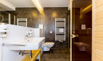A modern bathroom with a shower and a sauna. The walls are in dark tones, and there is a sink as well as towel holders.