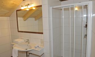 A modern bathroom with a sink, mirror, and a shower. The walls are tiled, and the ceiling features wooden elements.