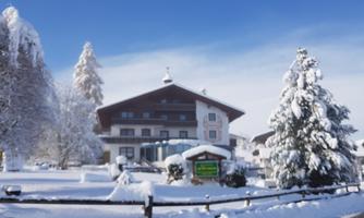 A traditional house in winter, surrounded by snow-covered trees. The sky is clear and blue, creating a peaceful winter landscape.