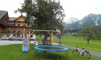 A playground with a trampoline, a swing, and a slide in a beautiful mountain landscape. Children are playing and having fun on the green grass.
