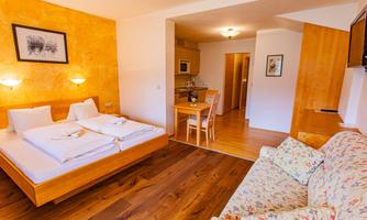 A cozy room with a double bed, a dining table, and a comfortable couch. The warm colors and wooden floors create an inviting atmosphere.