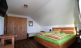 A cozy bedroom with a double bed and colorful bed covers. The room has wooden flooring and large windows that let in a lot of light.