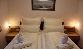 A cozy bedroom with two beds and large pillows. Next to the beds are wooden shelves and small bedside lamps.