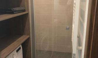 A modern bathroom with a shower and a washing machine. Wooden shelves provide space for towels and other utensils.