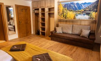 A cozy room with a large window and a beautiful view of the mountains. There is a sofa, a wardrobe, and a warm color scheme.