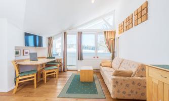 A bright and modern living room with a sofa and a table. Large windows provide plenty of natural light and a view outside.