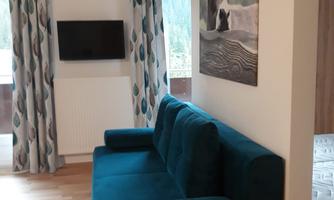 A modern living room with a blue sofa and a wall mural. In front of the sofa, there is a TV on the wall.