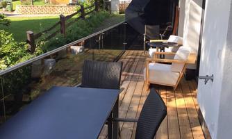 A beautiful balcony with a wooden table and elegant chairs. In the background, green trees and traditional houses can be seen.