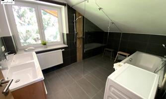 A modern bathroom with a large shower and a bathtub. Bright tiles and windows provide plenty of daylight.