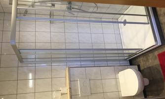 A modern bathroom with a shower cabin and a toilet. The walls are tiled and there is a small shelf space.