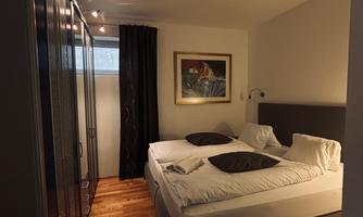 A modern bedroom with a double bed and a black wardrobe. The wooden floor and the artwork on the wall give the room a cozy atmosphere.