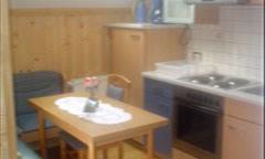 A bright kitchen with wooden details and modern design. A table with chairs is in the center, accompanied by a stove and cabinets.