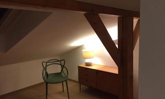 A cozy room under the roof with a chair and a sideboard. The soft lighting creates an inviting atmosphere.