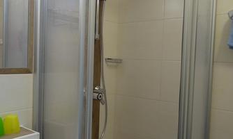 A modern bathroom with a glass shower cabin and a sink. The walls are light and neutral, and there is a large mirror.
