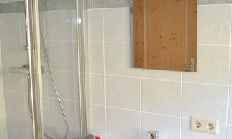 A modern bathroom with a shower and a white sink. A gray towel is casually laid on the sink, next to a mirror.