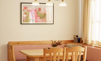 A cozy dining area with a wooden table and chairs. The walls are light, and a beautiful picture hangs above the bench.