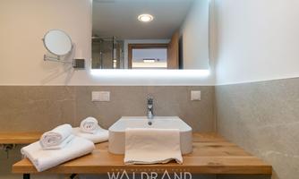 A modern bathroom with a stylish sink on a wooden shelf. Towels are neatly arranged, and a lit mirror complements the design.