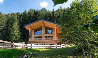 A modern wooden house surrounded by forests and meadows. The architecture is bright and welcoming with large windows that let in plenty of light.