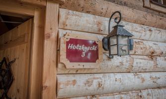 A wooden sign with the inscription "Holzknicht 3" hangs on a rustic wooden facade. Next to the sign is a stylish lantern.