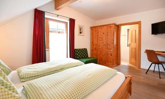 A cozy bedroom with two beds and checkered bedspreads. There is a wardrobe, a workspace, and a television.