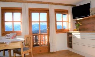 A cozy living kitchen with wooden windows and a view of the mountains. The light streams through the windows, giving the room a warm atmosphere.