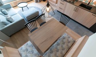 A modern kitchen with wooden details and a dining table. In the background, there is a cozy living area with a sofa.
