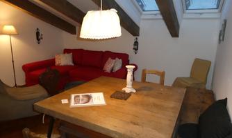 A cozy living space with a red sofa and a wooden table. Large windows under the roof provide plenty of light.