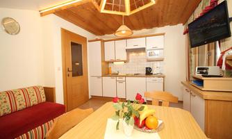 A cozy kitchen with a dining table and colorful furniture. In the foreground is a bowl of fresh fruit.