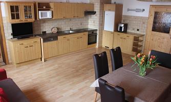 A modern kitchen with wooden cabinets and light surfaces. A dining area with a table and chairs is also visible.