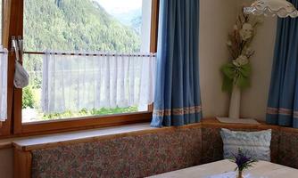 A cozy dining area with a wooden table and pretty chairs. Through the window, there is a view of green mountains.