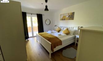 A bright bedroom with a large bed and yellow pillows. There is a balcony overlooking the outside and modern furniture.
